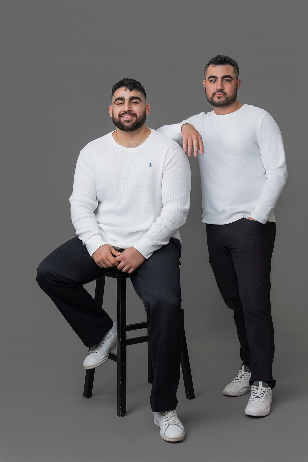 A series of studio portraits showing someone in a white sweater and black pants sitting on a stool against a gray background.