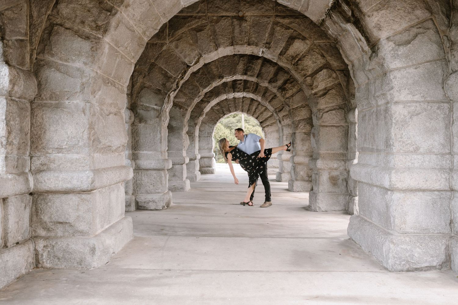 A couple embracing in front of an ornate stone archway with decorative pillars and architectural details.