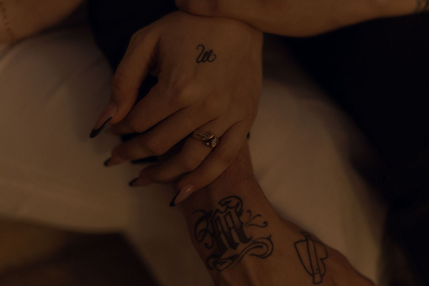 close up m/f arms - f holding his arm and they have tattoos and a wedding ring