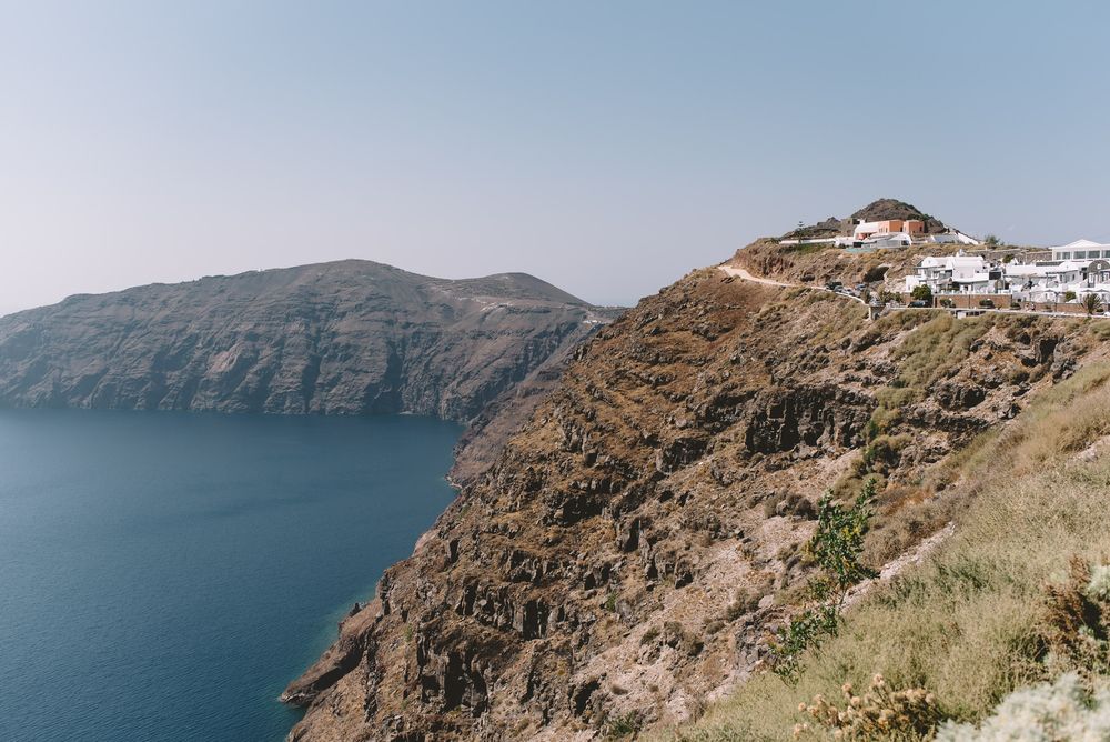 Panoramic view of white buildings perched on cliffs overlooking the deep blue Mediterranean Sea in Santorini, Greece.
