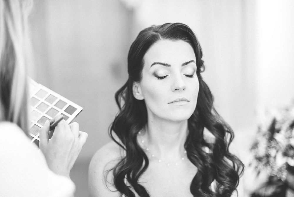 Bridal beauty session showing preparation and makeup application with closed eyes and elegant curled hairstyle.