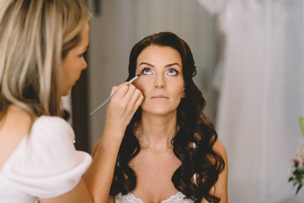 A bride getting ready for her wedding with professional hair and makeup being styled in a romantic, elegant setting.