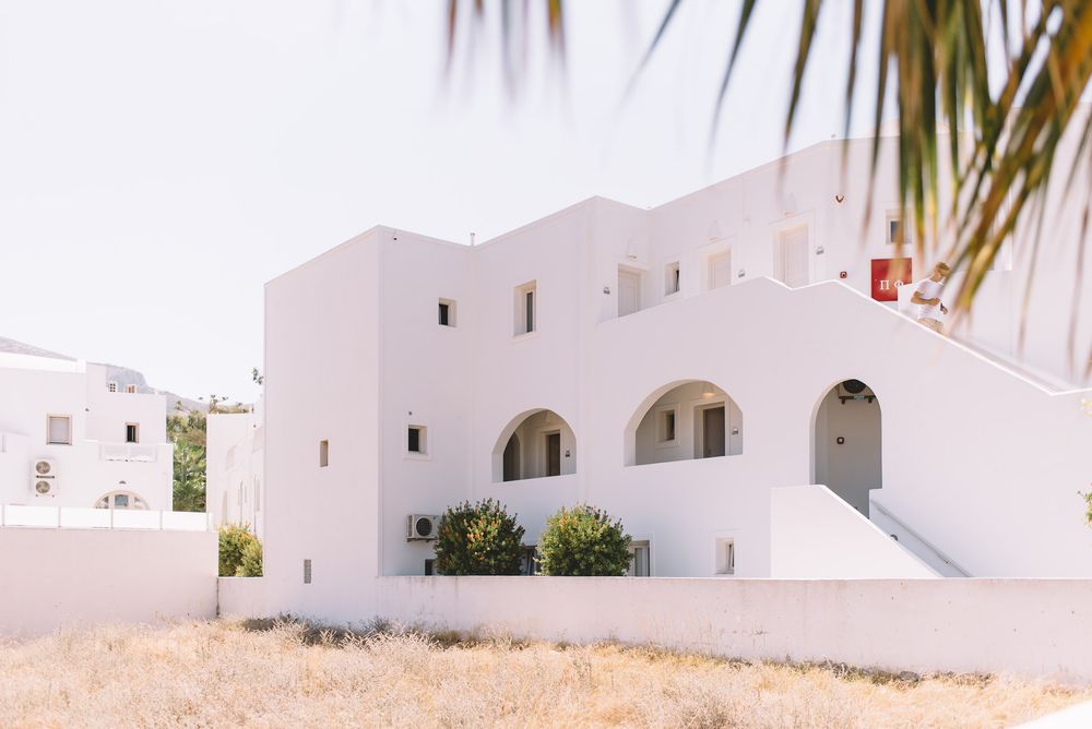 White Mediterranean style buildings with arched windows and doorways sit along a winding path under a sunny sky.