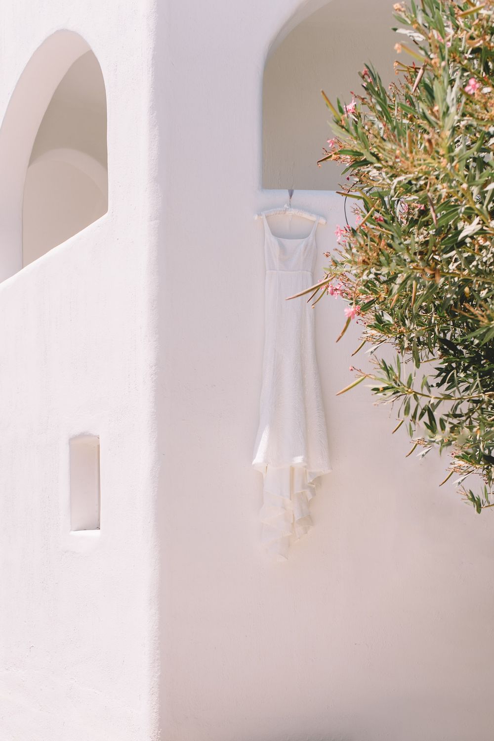 Minimalist white archway with delicate olive branches casting soft shadows against a sunlit Mediterranean wall.