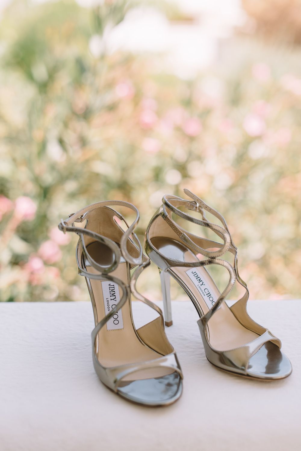 Metallic silver designer wedding sandals arranged artistically against a soft floral background.