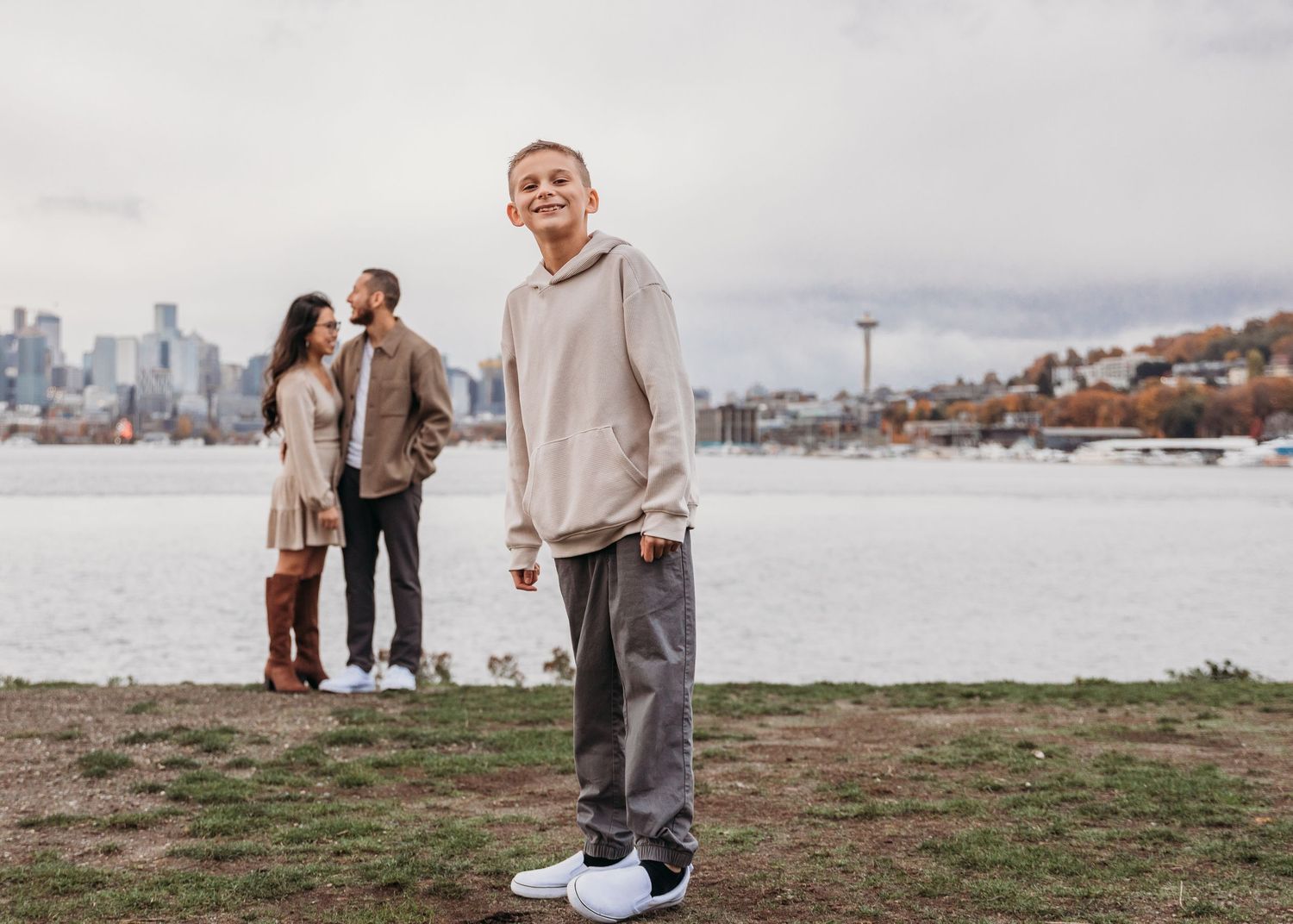 A cozy engagement photo session on a waterfront with the city skyline visible in the background on a cloudy day.
