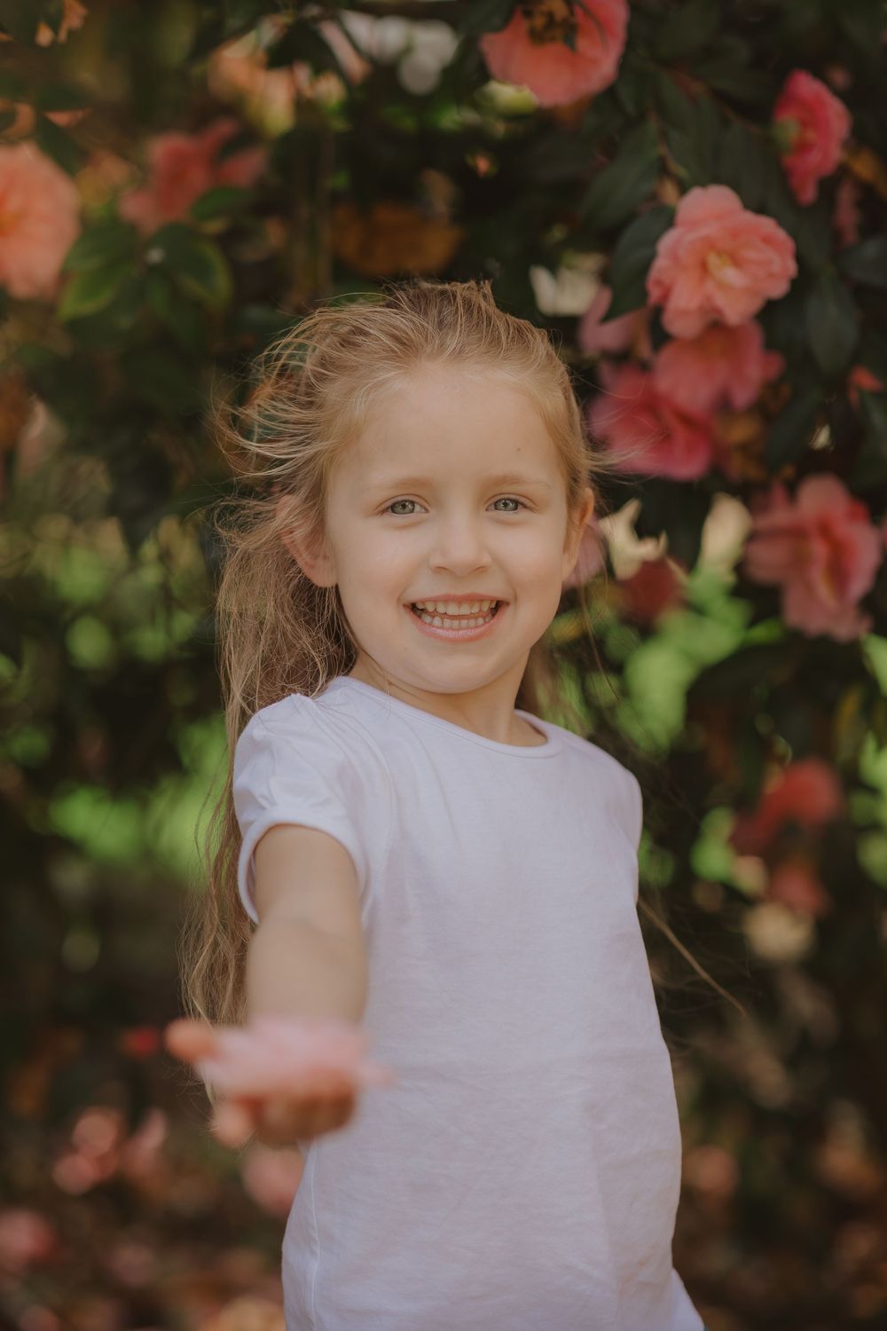 A candid springtime portrait with pink flowers and a white t-shirt against a natural garden backdrop.