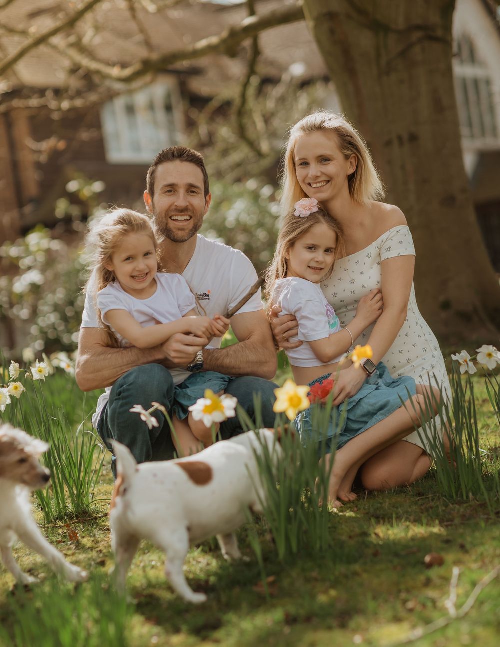 Family and dog enjoying a spring day together among blooming daffodils in a garden setting.