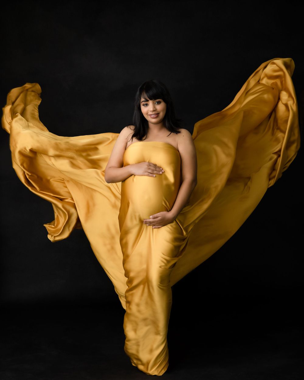 Artistic maternity photo with billowing golden fabric creating wing-like effect.