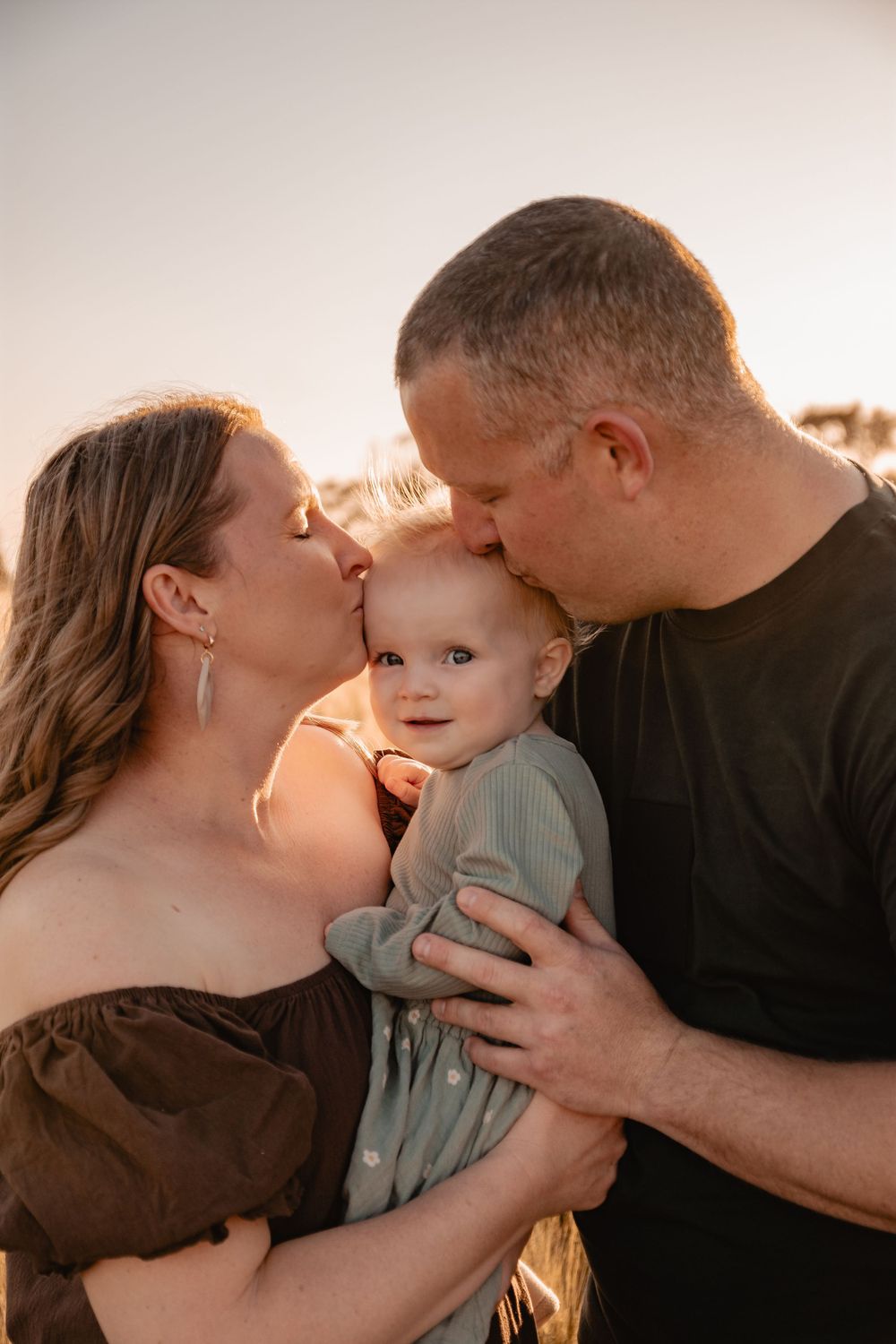 mum and dad kissing baby on the head