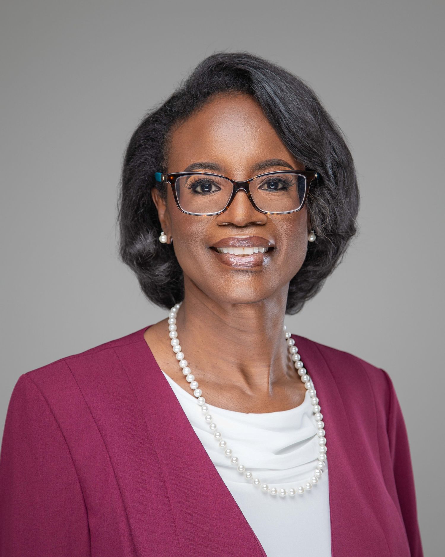 Professional portraits of a person in a burgundy blazer and pearl necklace against a gray backdrop.