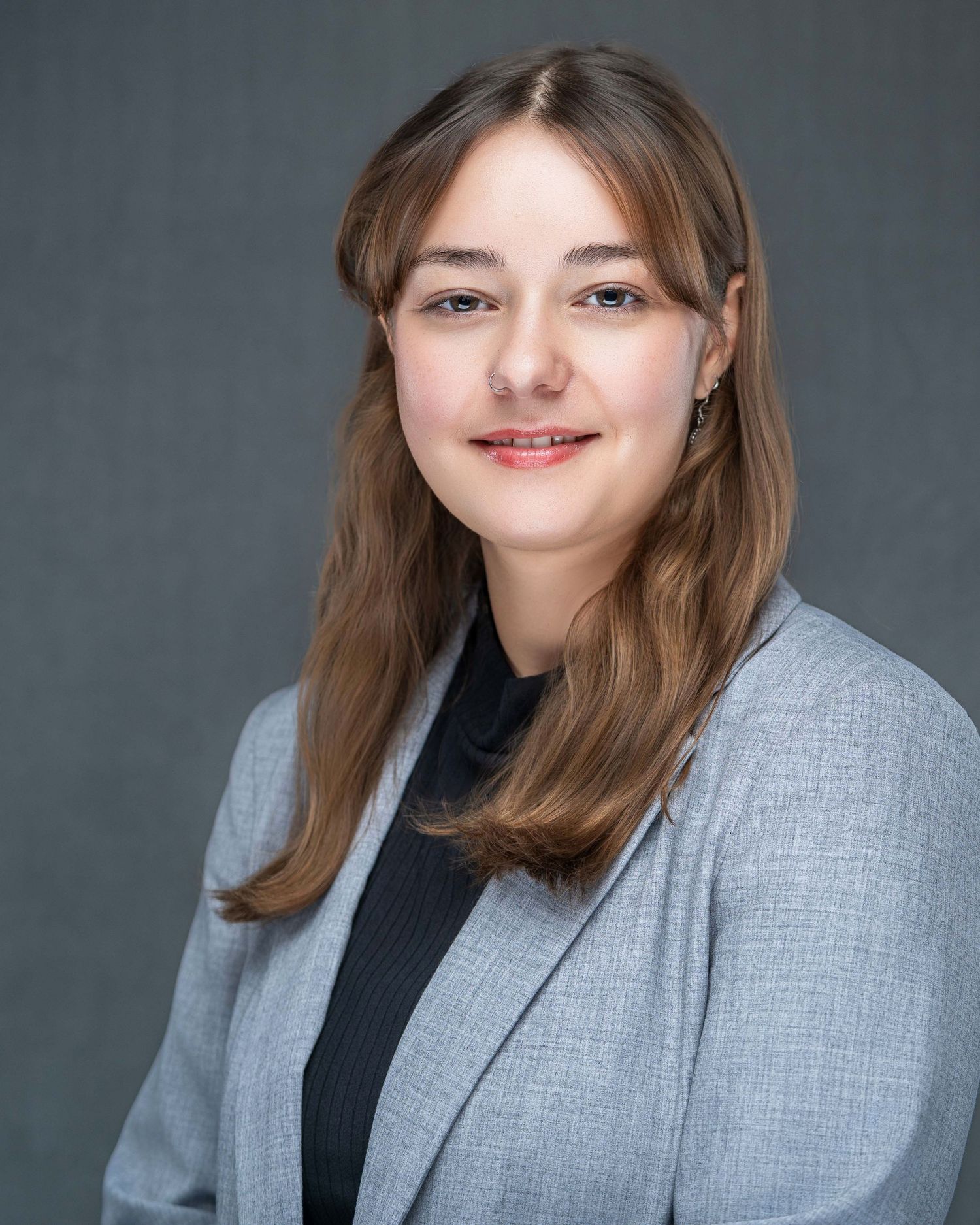 Professional portrait in gray blazer and black turtleneck against dark background.