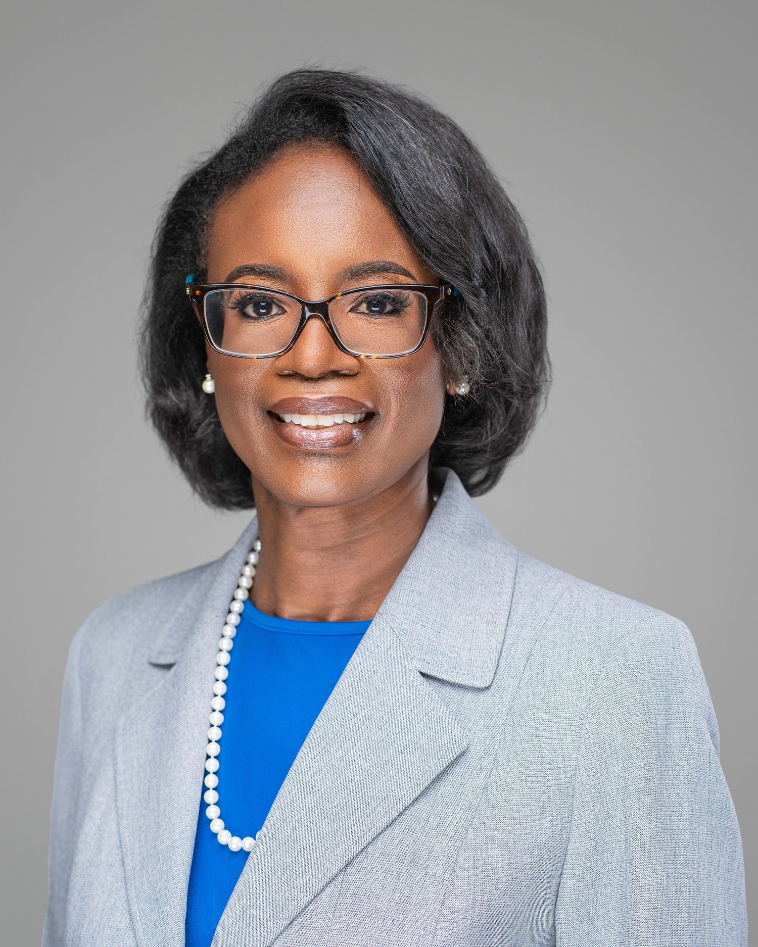 Professional headshots of a person wearing a light gray blazer and blue top against a gray background.