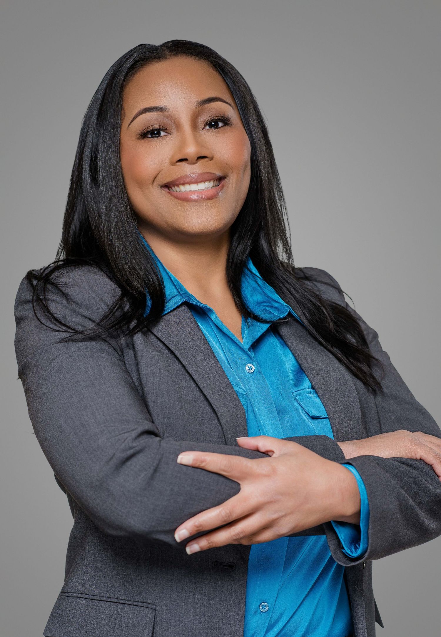 Corporate headshot of a businesswoman wearing gray blazer and blue blouse with a welcoming smile.