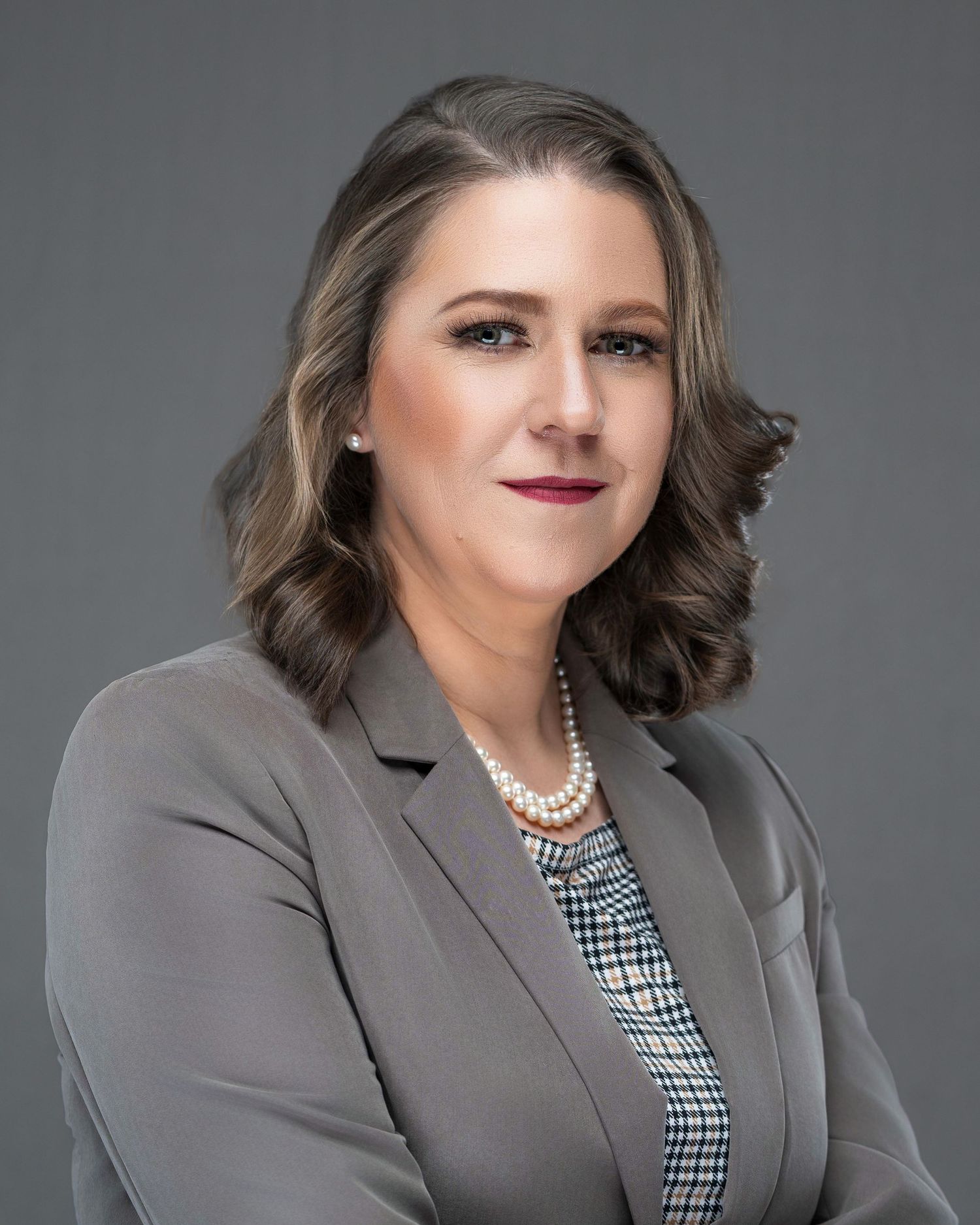 Professional headshot of person wearing gray blazer and houndstooth top with pearl necklace.