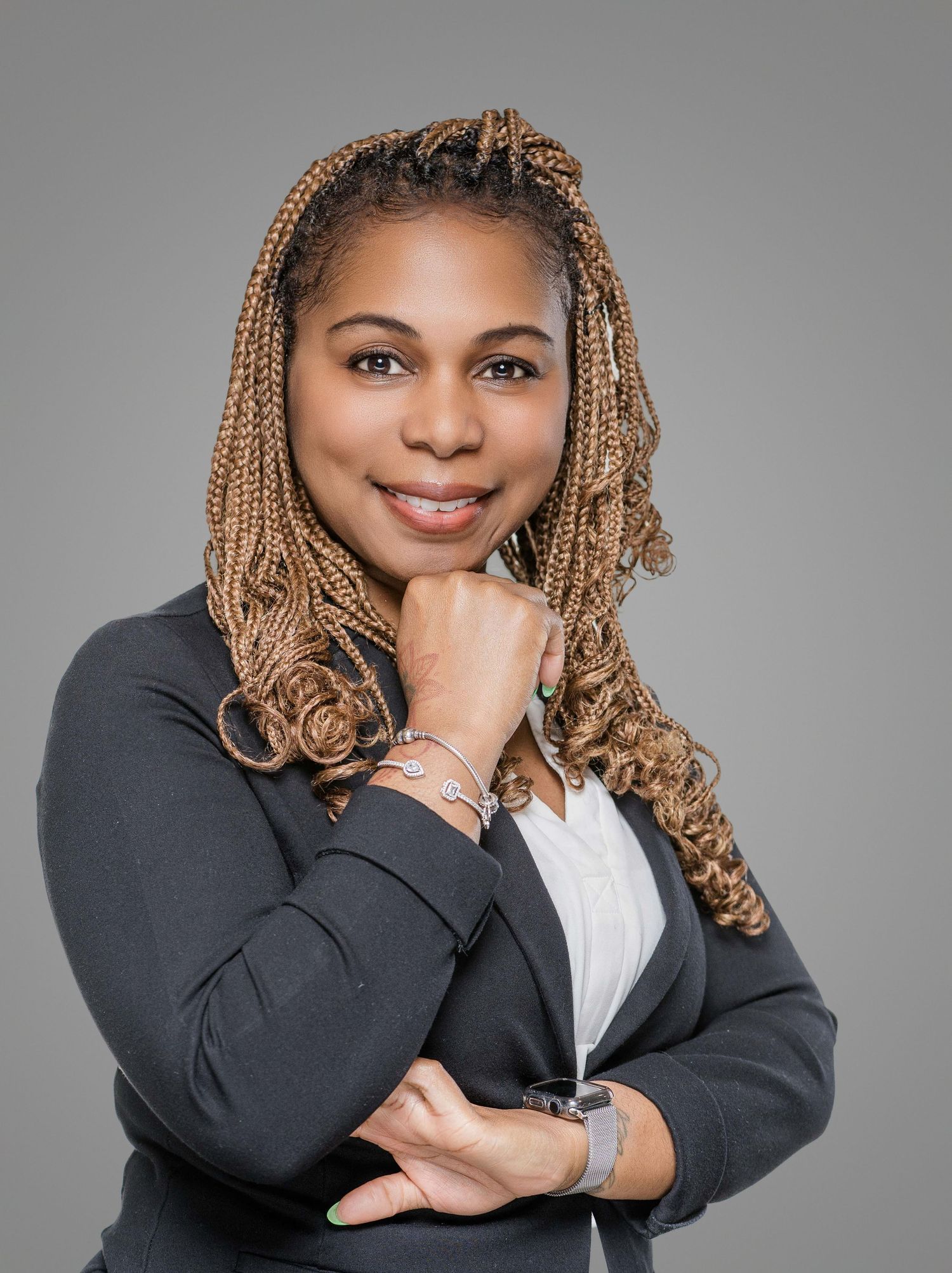 Professional headshot of a businesswoman in a black blazer with blonde box braids and a warm smile.