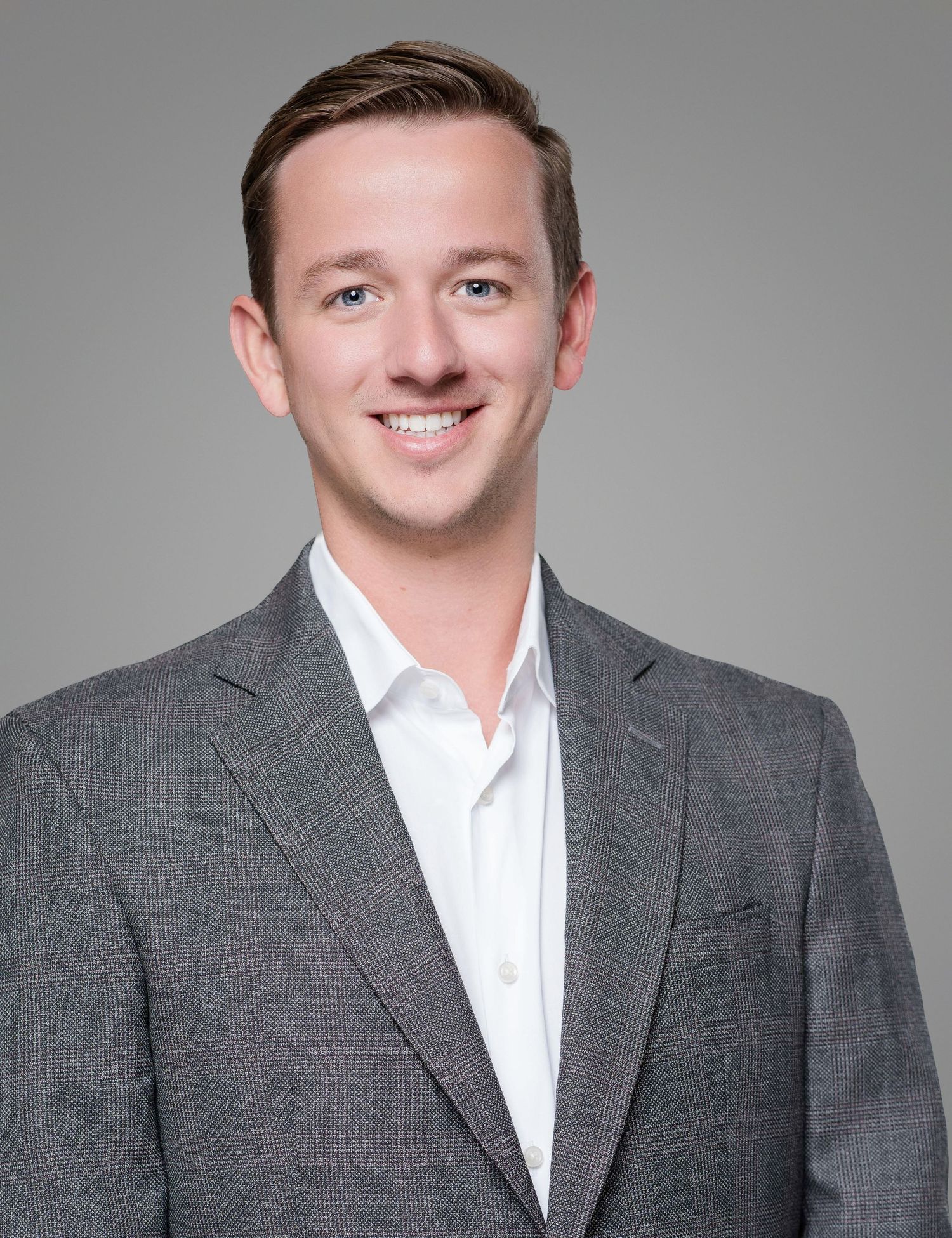 Professional headshot of a businessman in a gray suit jacket and white shirt against neutral background.