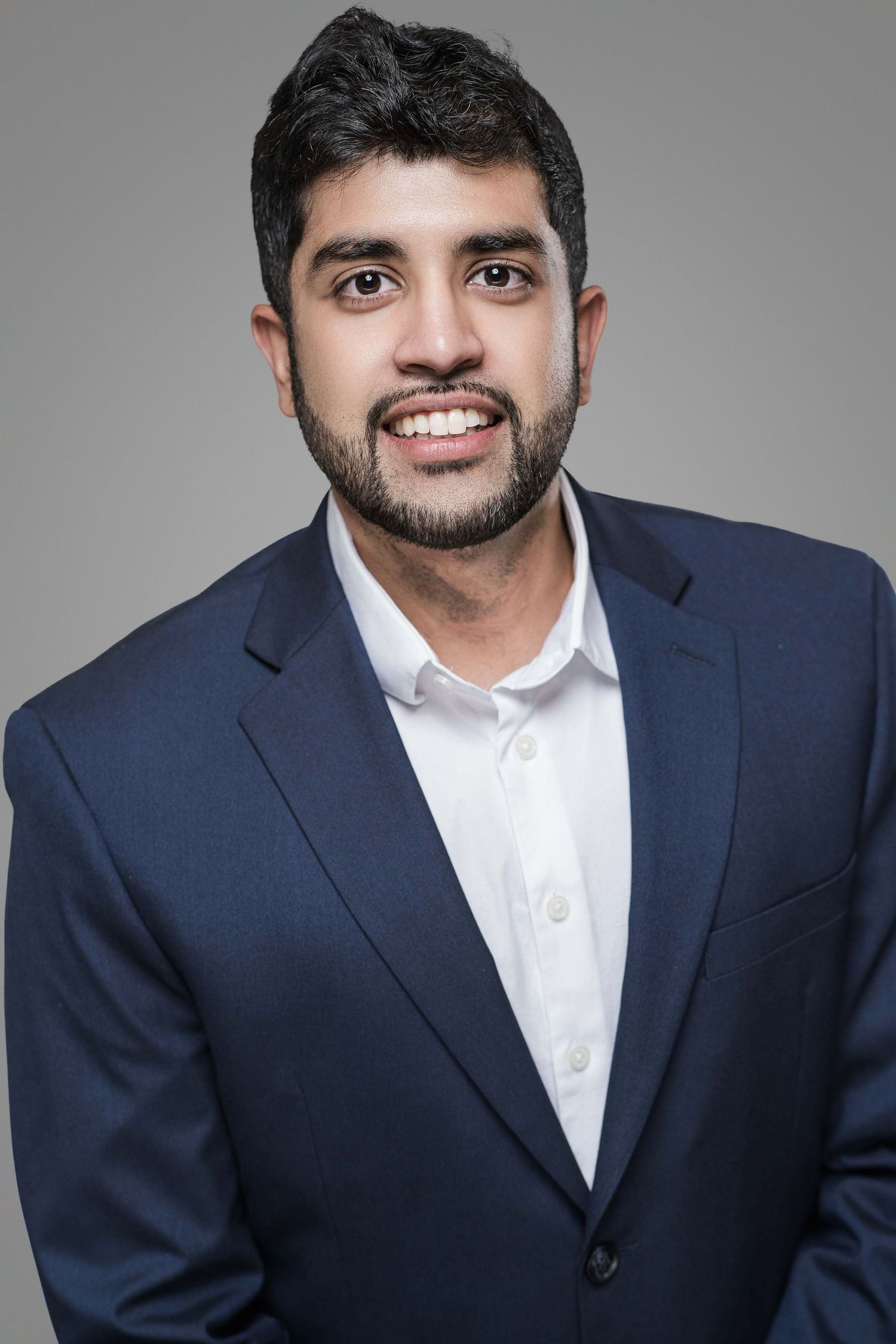 Professional headshot of a businessman in navy suit jacket with white shirt against gray background.