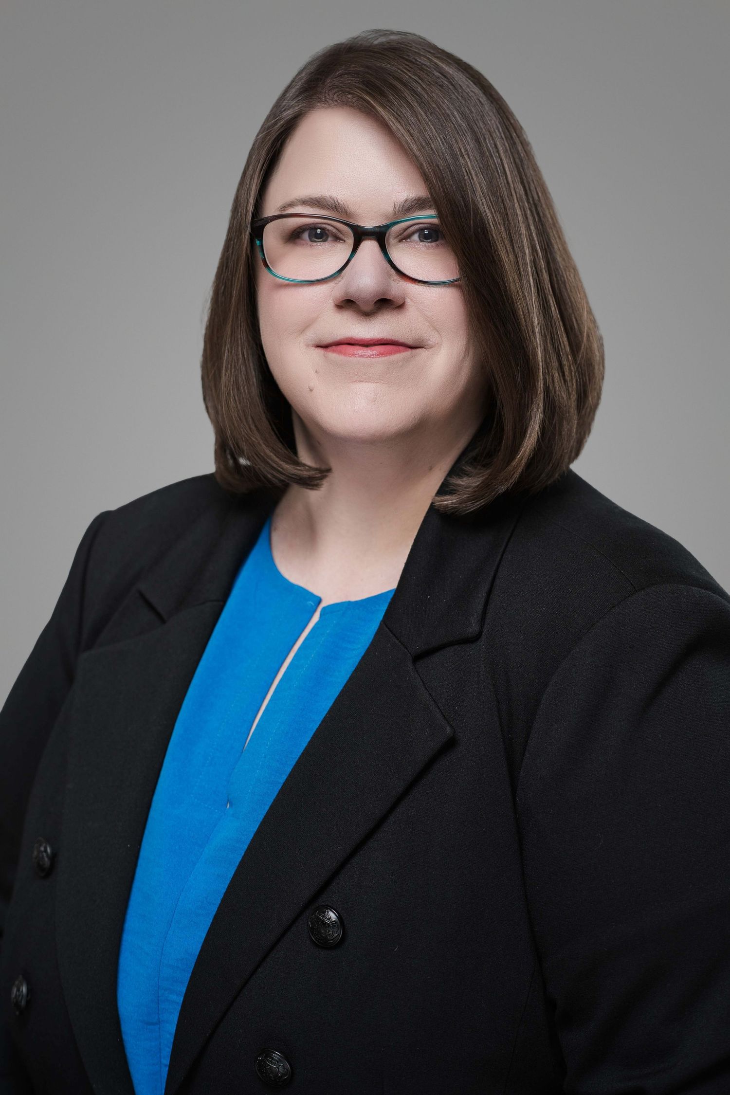 Professional portrait of a businesswoman in black blazer and blue top wearing glasses.