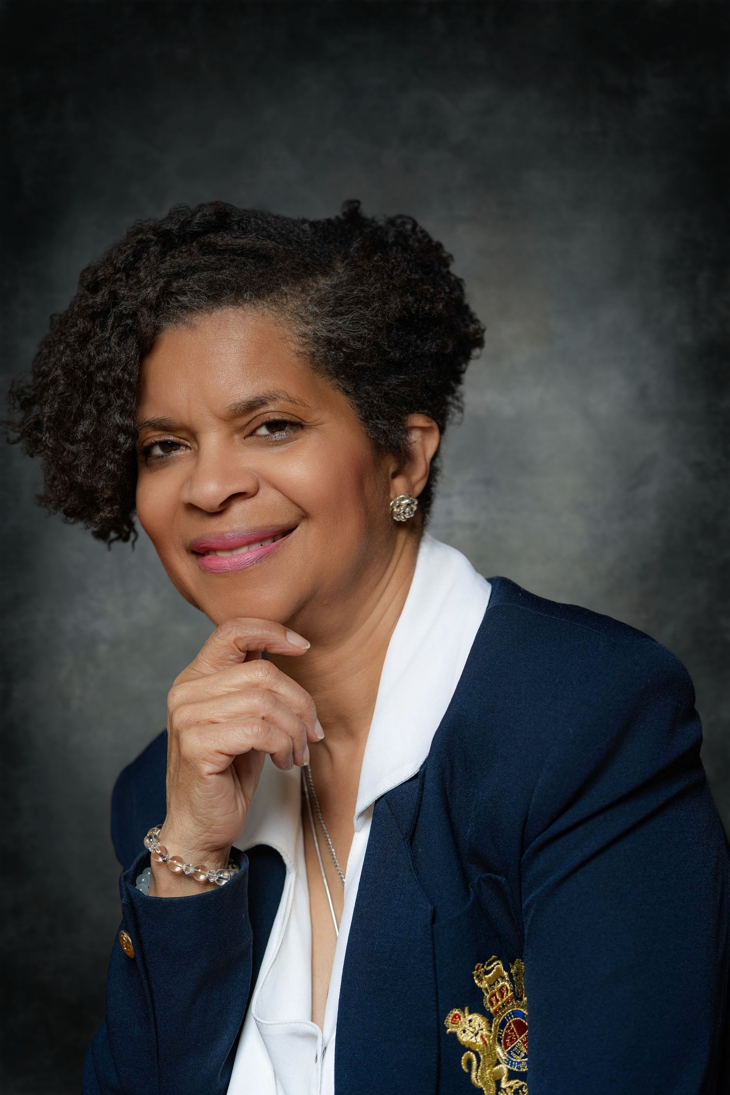 Professional headshots of person in navy blazer with gold brooch against dark background.