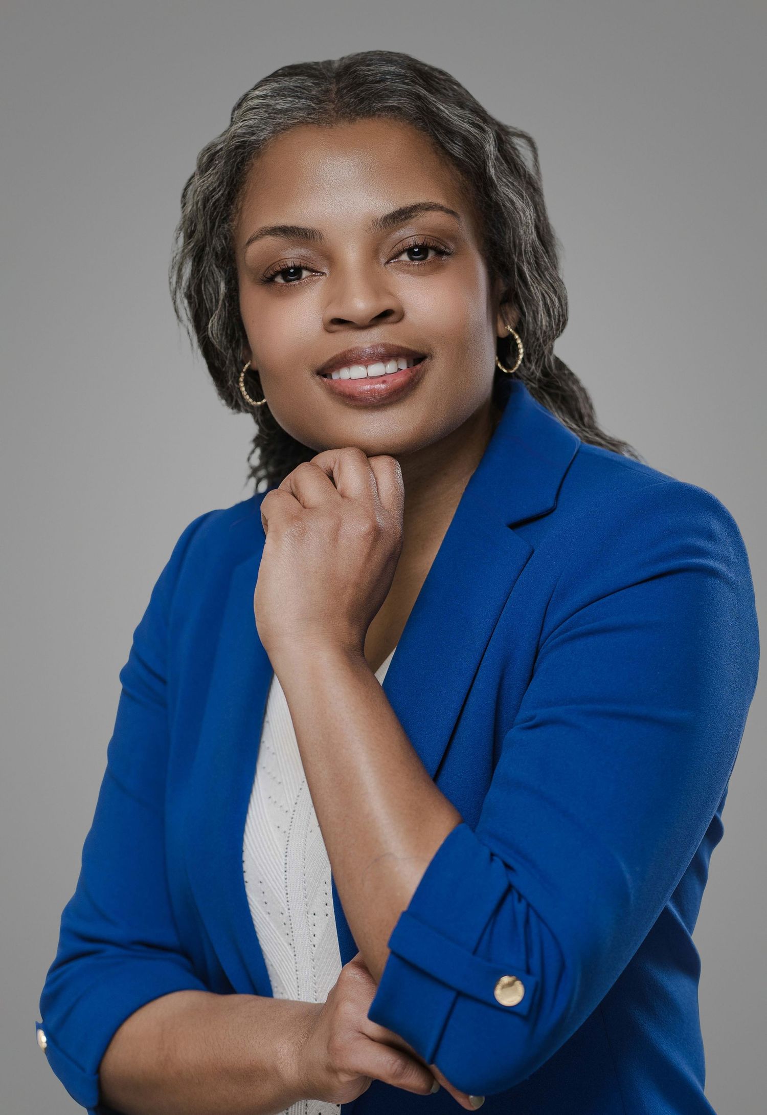 Professional portrait of a businesswoman in royal blue blazer with a warm smile and hand on chin.