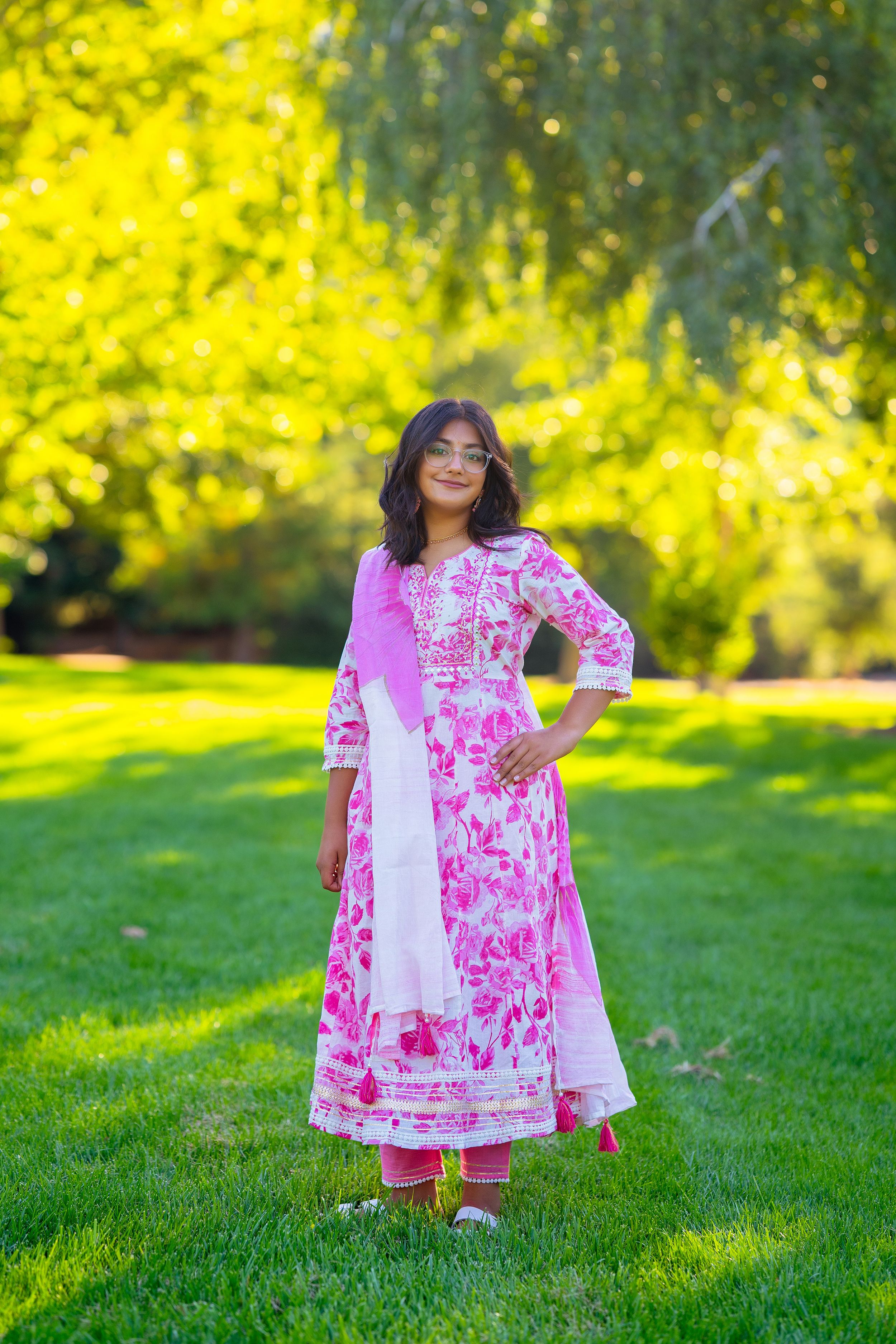 A pink and white floral anarkali dress with matching pants stands out against a sunny garden background.