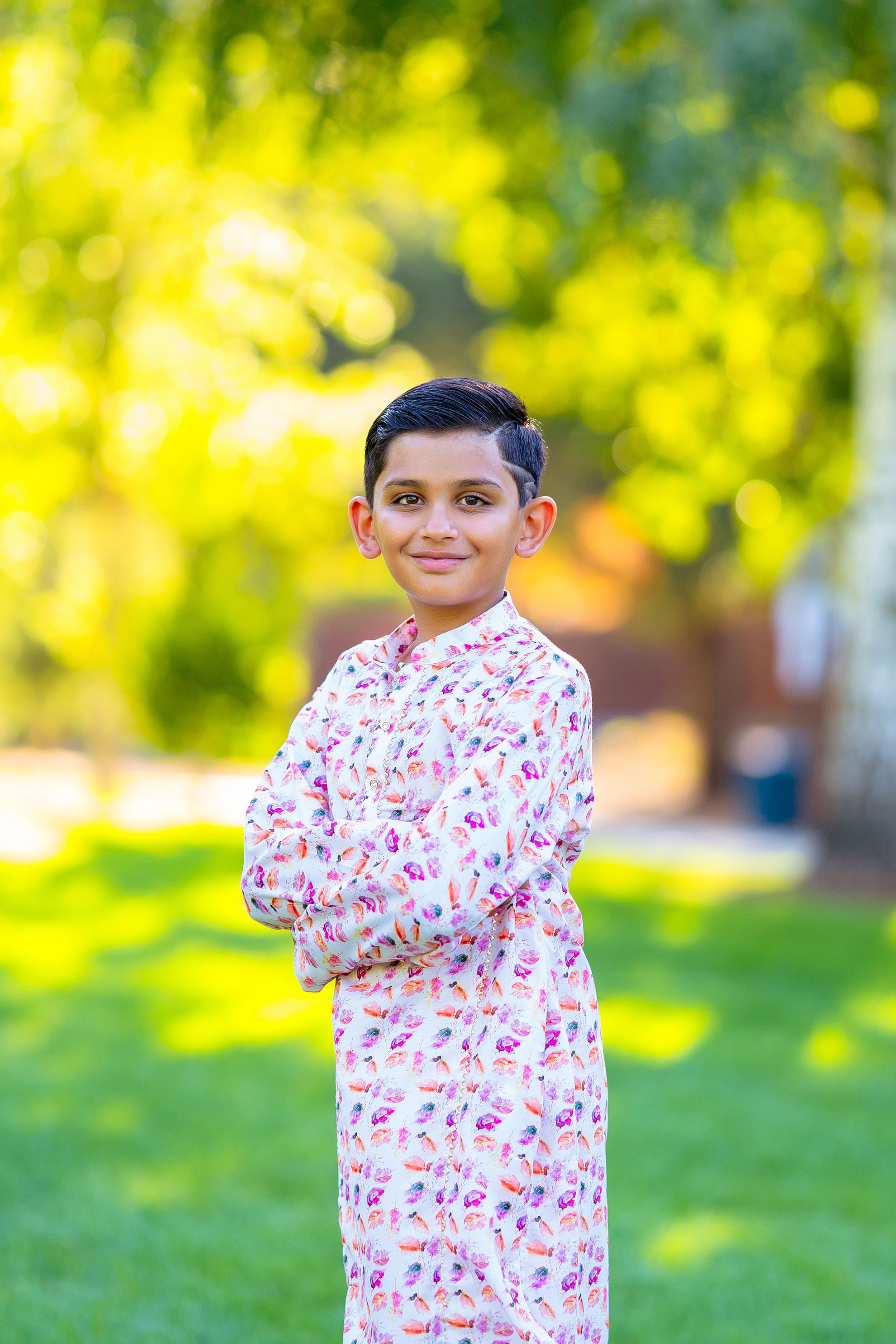 Child wearing a white patterned pajama set poses with arms crossed in a sunny outdoor setting with bokeh background.