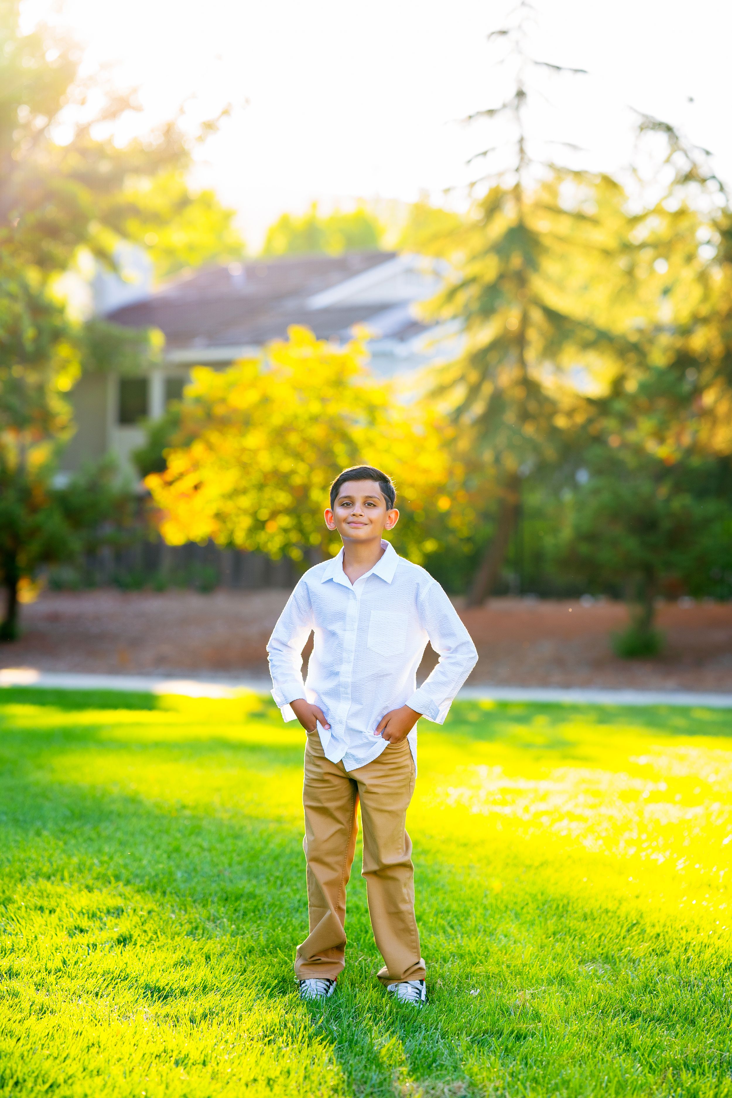 A young person stands confidently on green grass wearing a white shirt and khaki shorts on a sunny afternoon.
