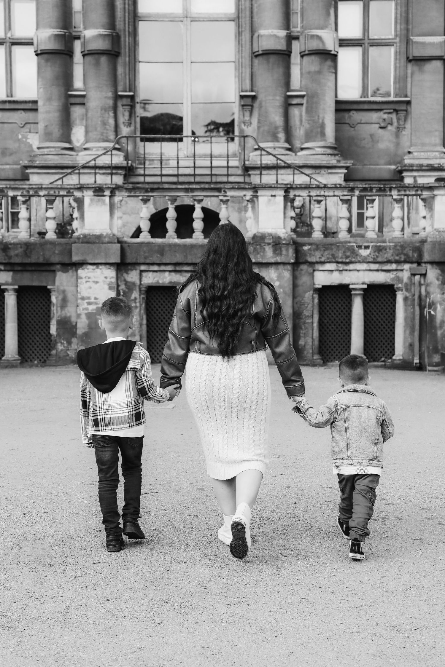 Family walking together through grand historic building courtyard in black and white photograph during family shoot in Nottingham