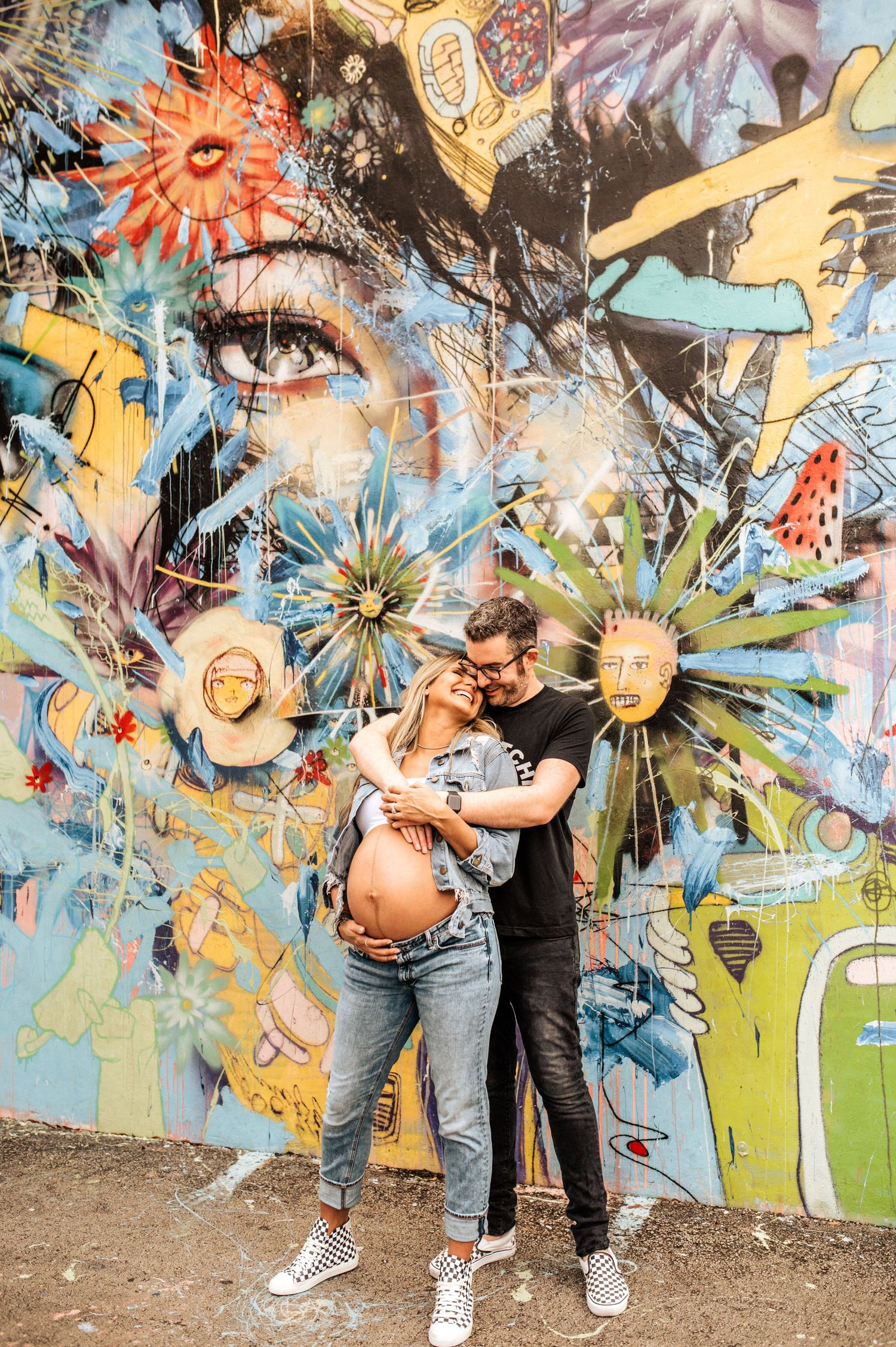 A maternity photo of a couple posing against vibrant street art with sun and flower designs.