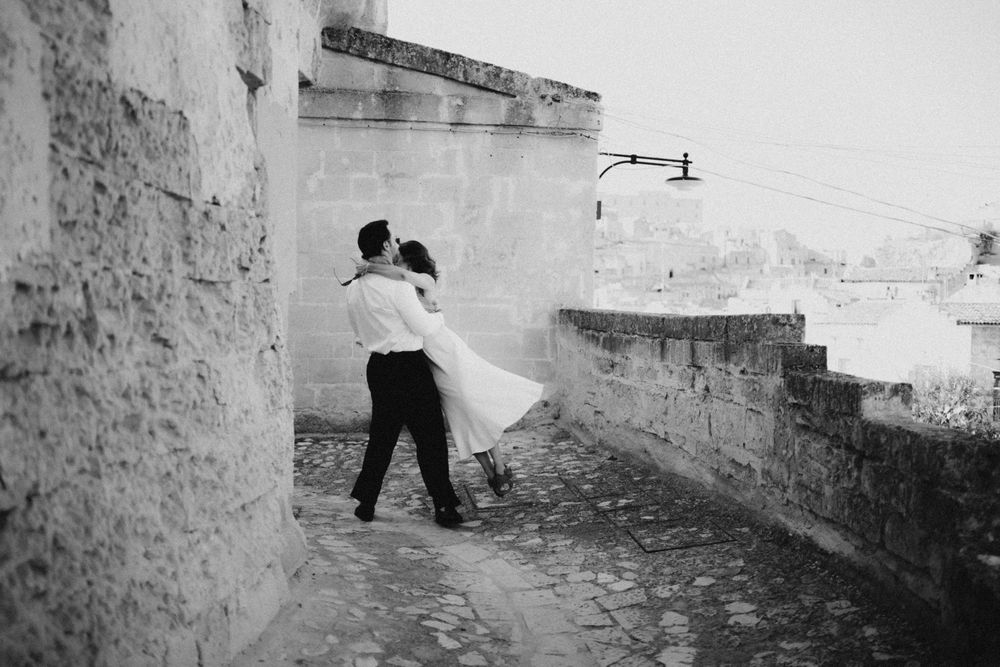 A romantic black and white photograph of a couple dancing on a stone terrace overlooking a city.