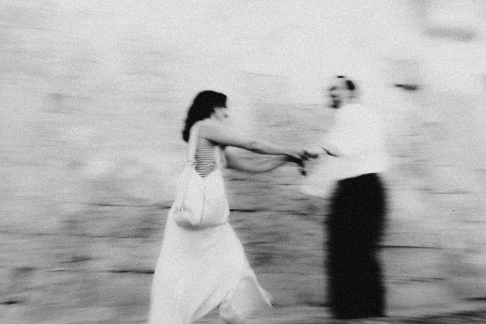 A blurred motion shot of a couple dancing joyfully in black and white.