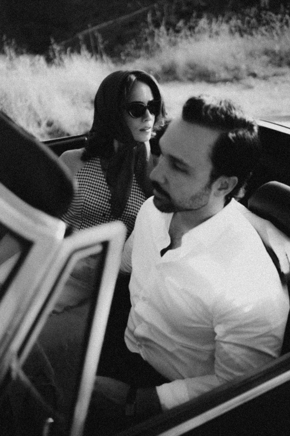 A black and white photo of a couple in a convertible car with a romantic vintage aesthetic.