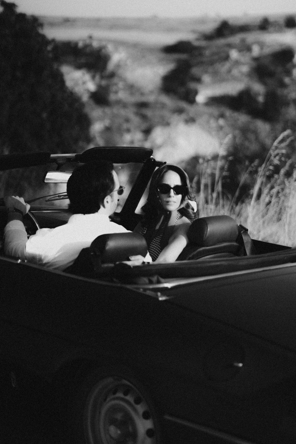 A stylish couple enjoying a drive in a classic convertible car along a scenic coastal road.