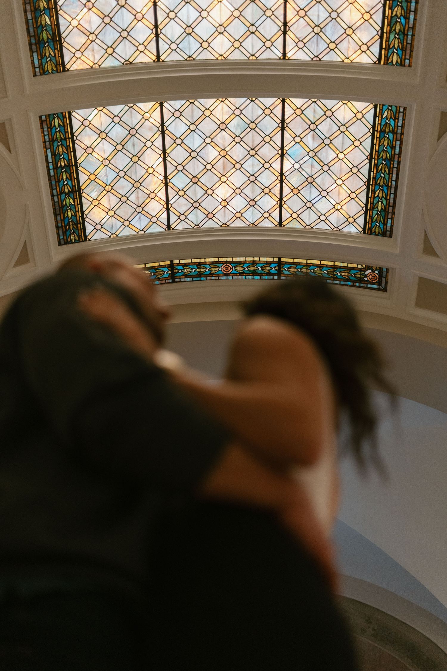 Curved stained glass windows with geometric patterns decorate an arched ceiling in warm ambient lighting.