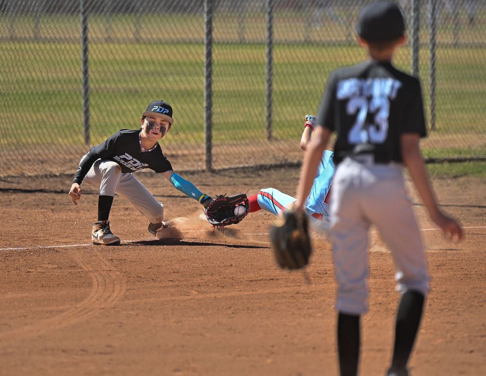 Young baseball player slides into base as fielder attempts tag during youth baseball game.
