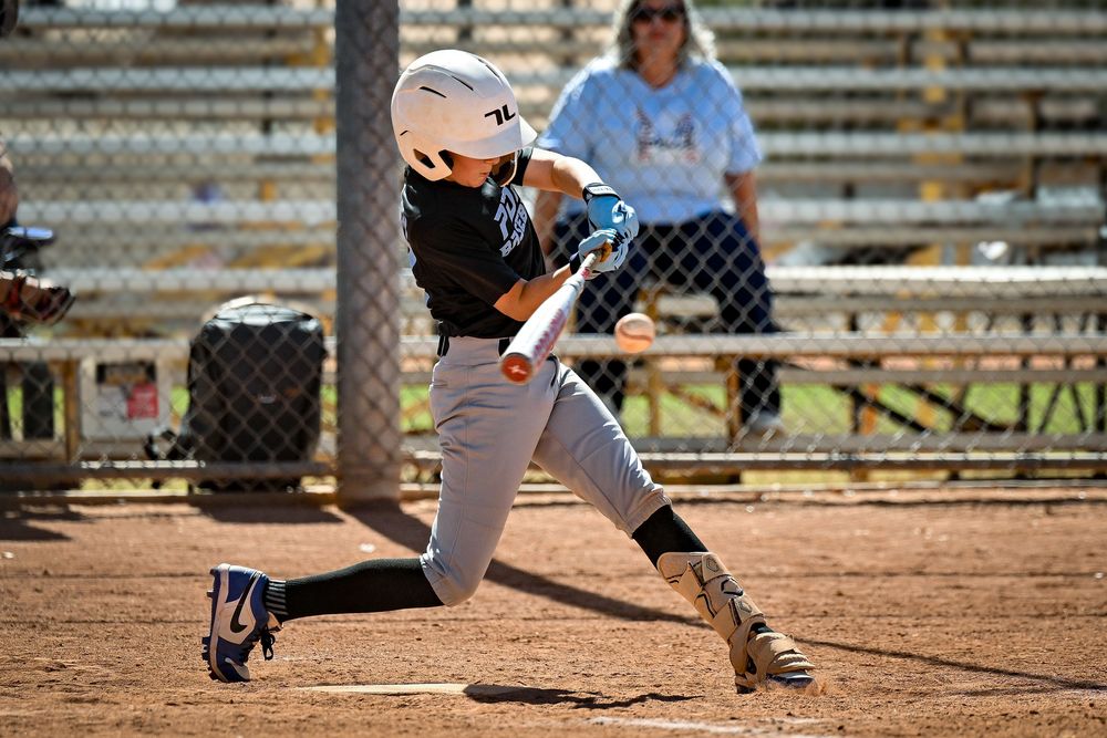 Young baseball player in white uniform swings bat at pitch during youth baseball game.