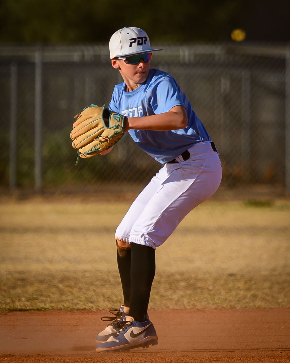 Young baseball player in blue PDP uniform crouches in ready position while playing infield defense.