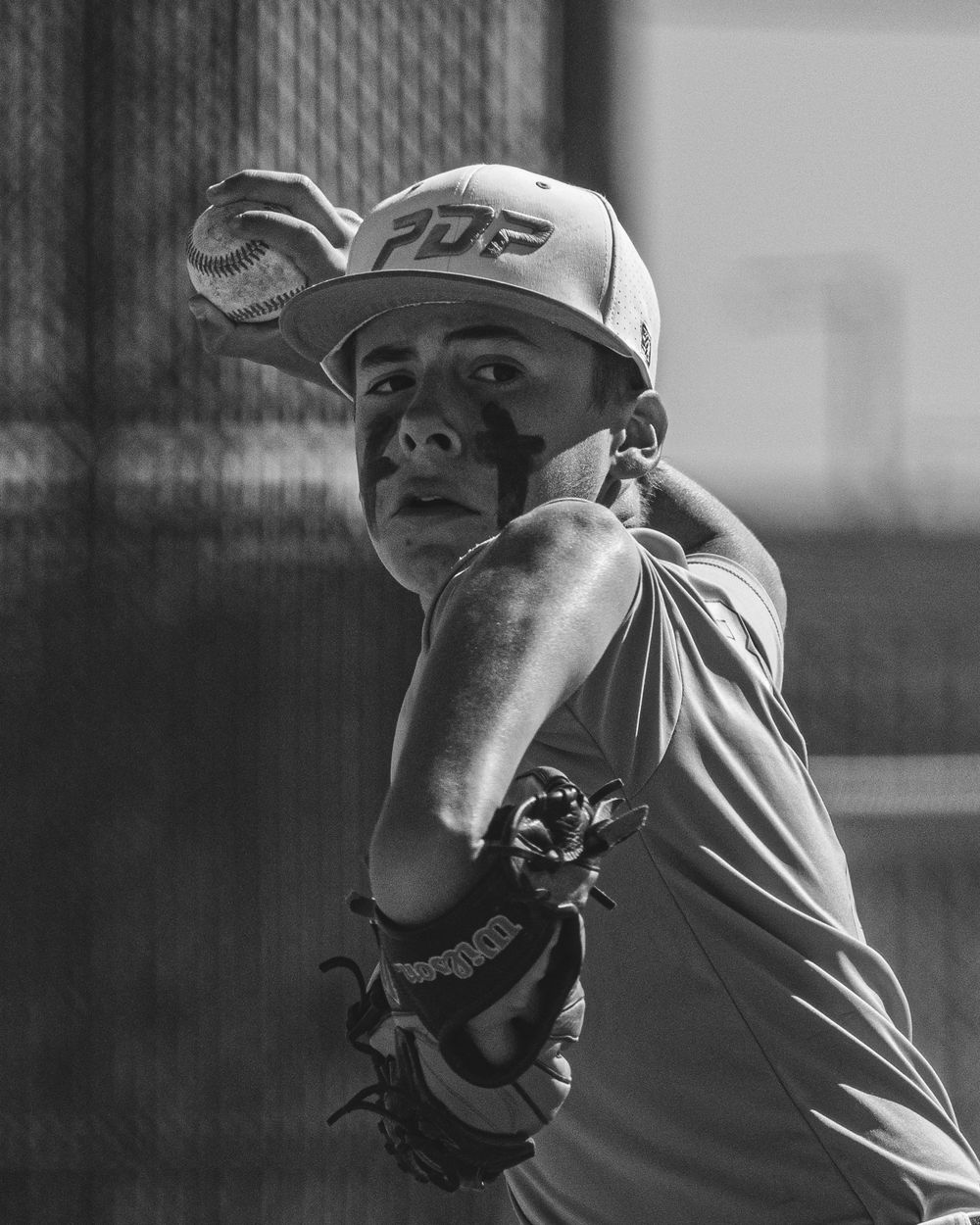 Black and white photo of a young baseball pitcher in PDP cap preparing to throw a pitch.