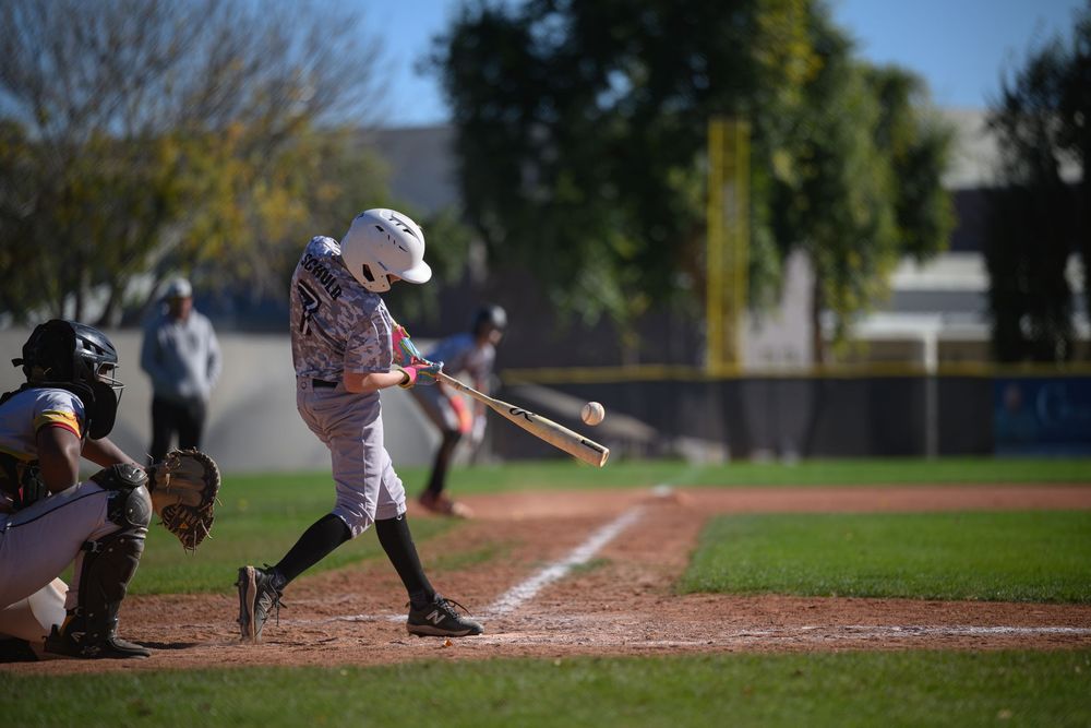Young baseball player swinging bat at home plate during a sunny outdoor game with catcher and umpire behind.