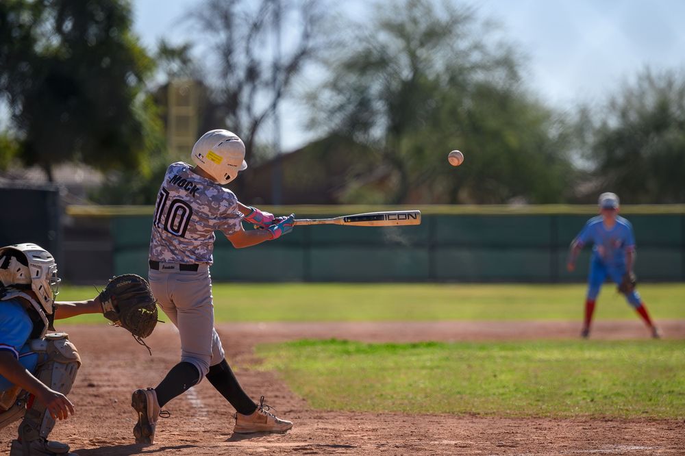 Youth baseball player number 10 swings bat making contact with ball, catcher and umpire behind home plate.