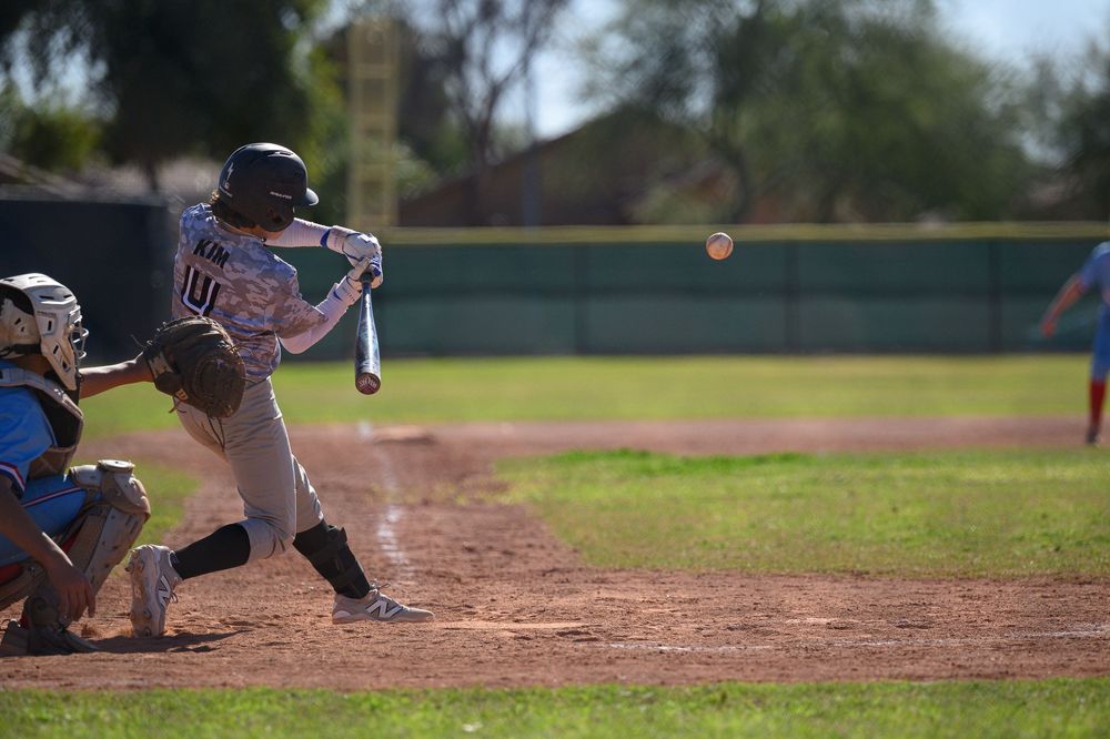 Baseball batter swinging at pitch during youth game, catcher crouching behind home plate on sunny day.