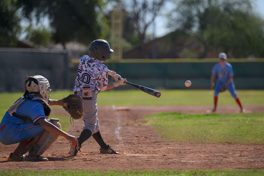 Youth baseball batter swinging at pitch with catcher crouching behind home plate during little league game.
