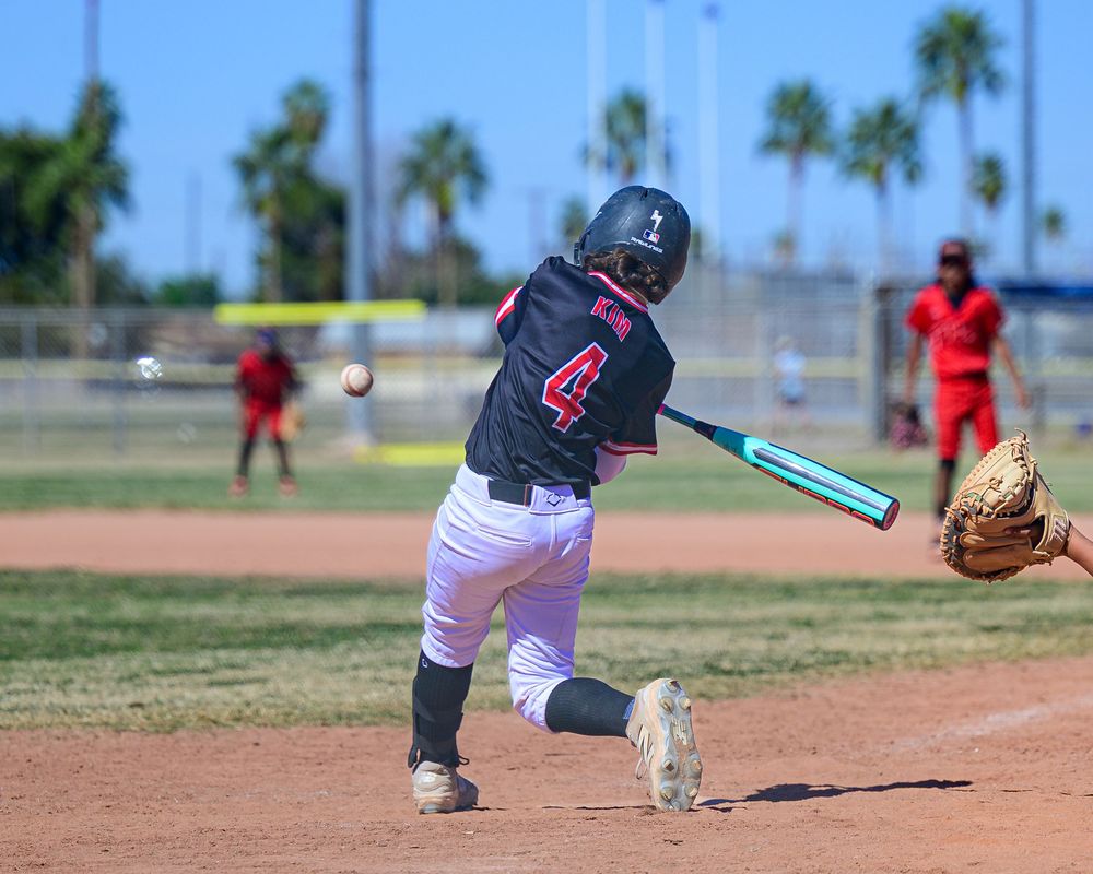 Youth baseball player wearing number 4 swings a teal bat at an incoming pitch during a sunny outdoor game.