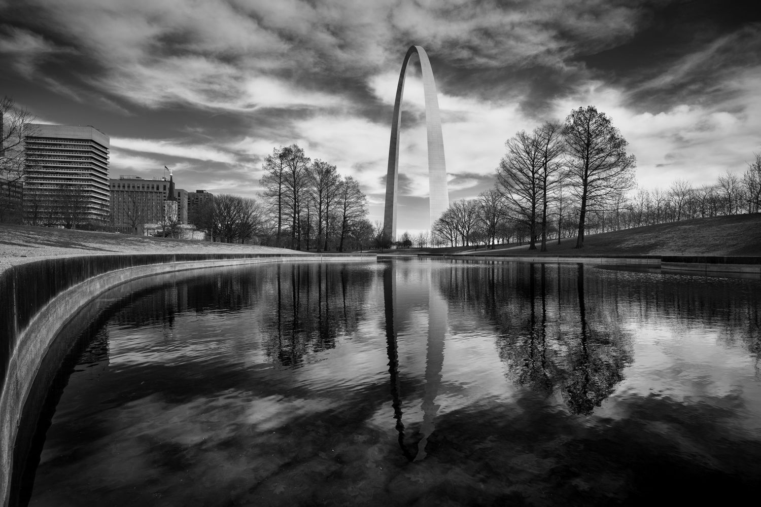 Dramatic black and white panoramic cityscape with storm clouds reflecting in calm water along urban waterfront.