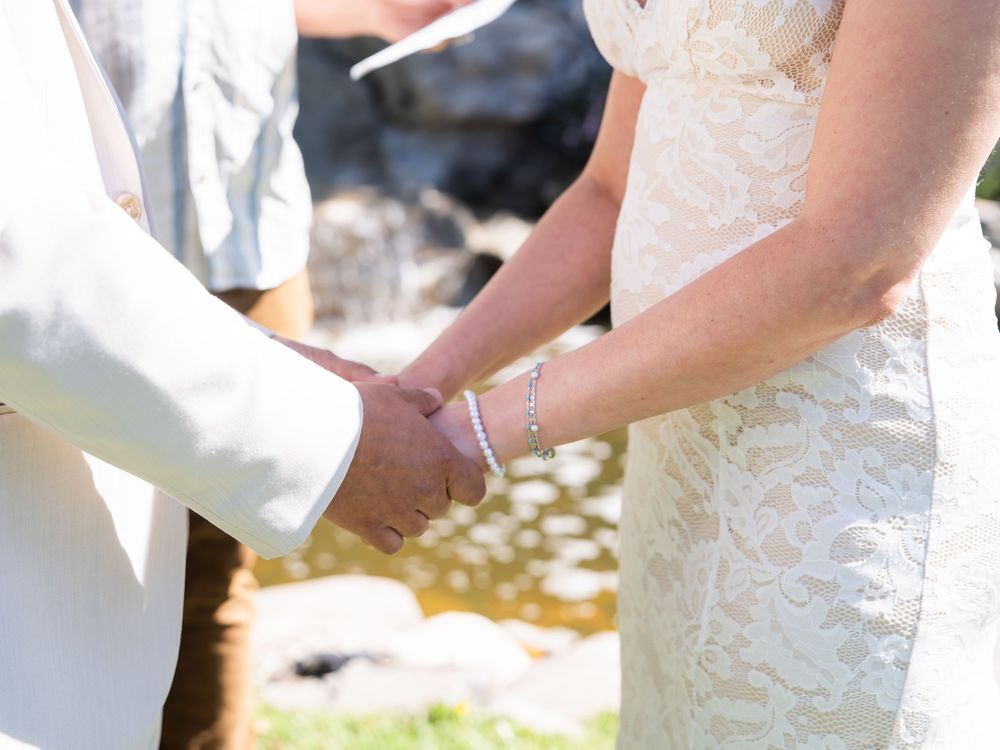 Close-up view of hands cutting a white wedding cake with floral decorations at an outdoor reception.