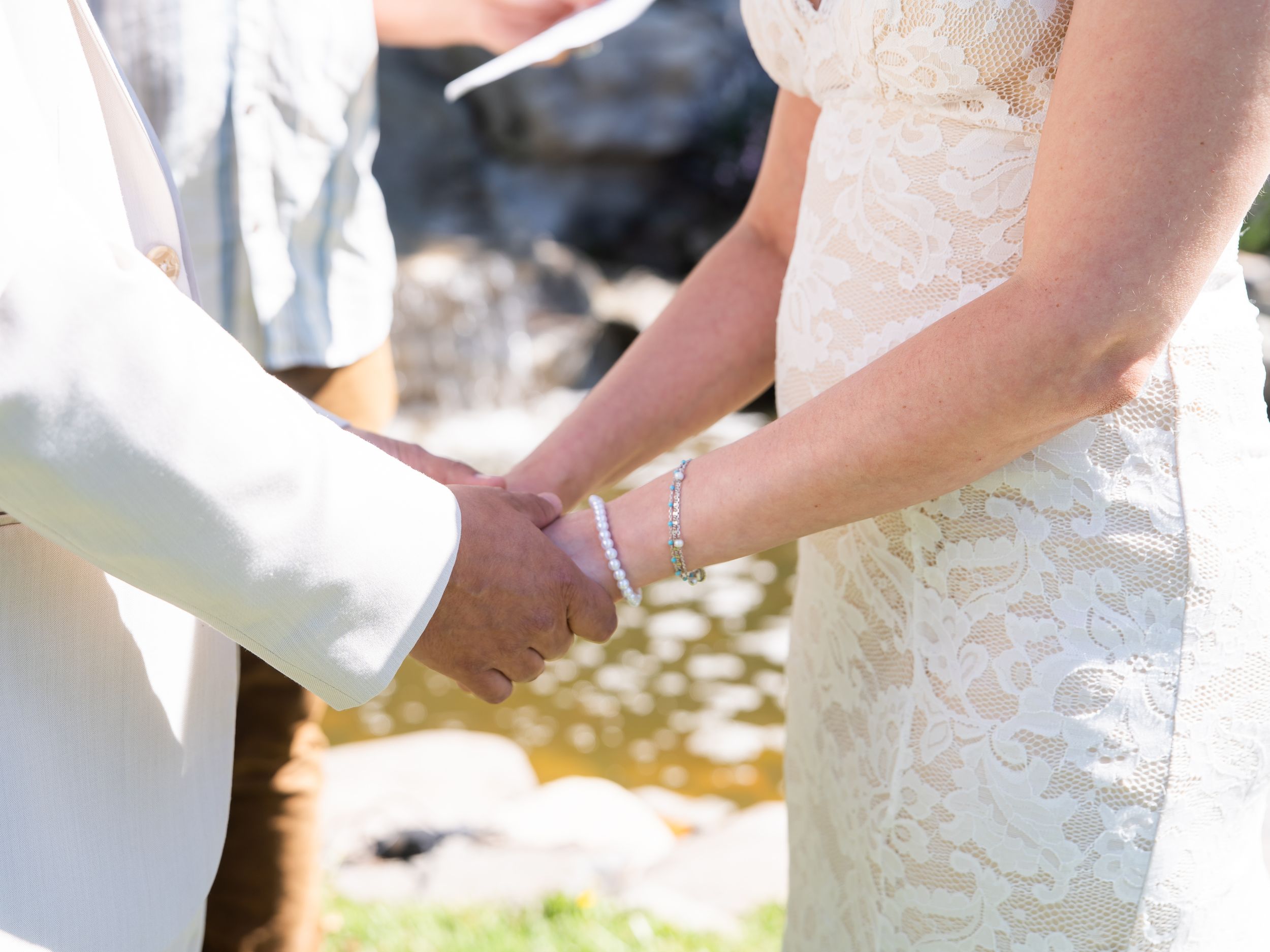 Close-up view of hands cutting a white wedding cake with floral decorations at an outdoor reception.