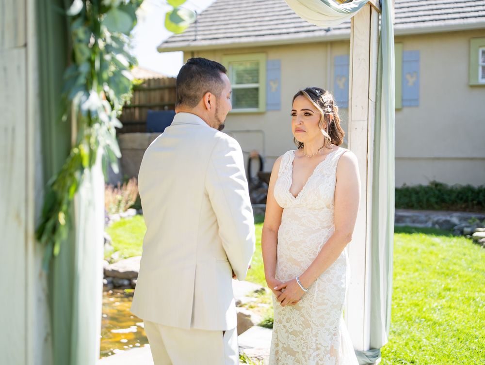 A bride and groom share a moment in white attire during their first look outside on a sunny garden lawn.