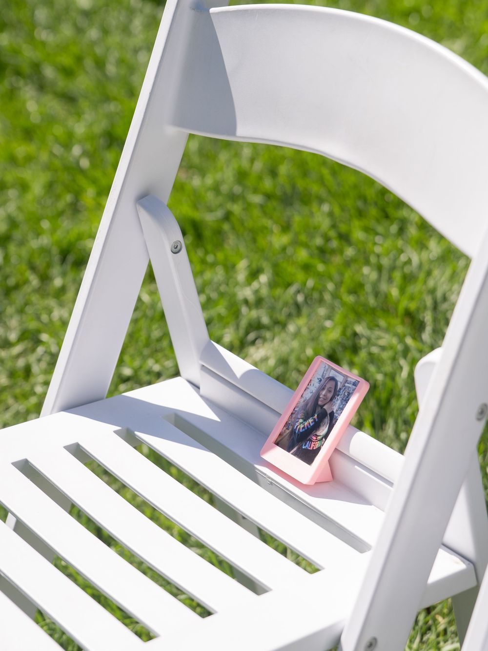 A simple white wooden lawn chair sits empty against a bright green grass background.