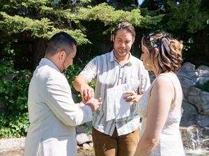 An outdoor wedding ceremony taking place in a garden setting with a waterfall feature in the background.